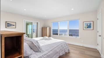 Un dormitorio con cama, mesita de noche de madera, armario y un amplio ventanal con vista al océano.