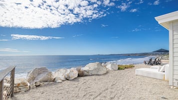 Vista de una playa con un edificio blanco, un sofá blanco y una valla de madera.