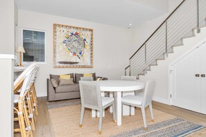 A modern living room with a round dining table, white chairs, a grey sofa, and a large abstract painting on the wall.