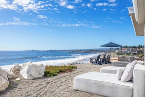 A beachside seating area with a view of the ocean, a patio umbrella, and a white couch.