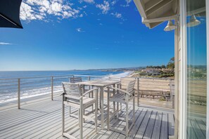 A wooden deck with white chairs overlooking a beach and ocean.