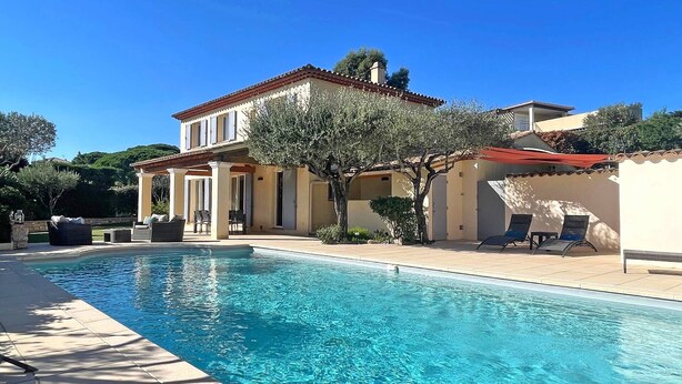 Un espace aménagé au bord d’une piscine, comprenant une piscine, des sièges d’extérieur et un bâtiment doté d’un toit en tuiles.