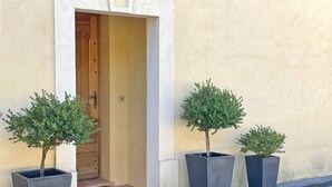Une entrée d’immeuble avec une porte en bois, trois arbres en pot et un mur en béton.