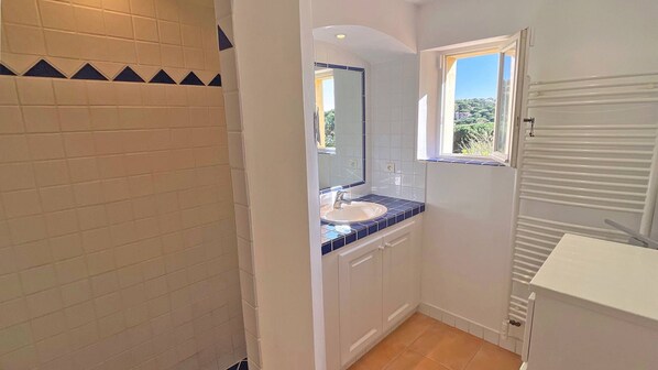 Un baño con lavamanos blanco, azulejos azules, un espejo y una ventana.