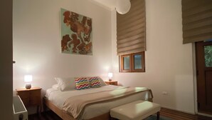 Una camera da letto con un letto di legno, una panca, un comodino con una lampada, un quadro appeso al muro e una finestra con persiane.
