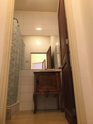 A narrow bathroom with a wooden cabinet, a shower curtain, and tiled walls. - Castelletto Bed and Breakfast (Santiago)