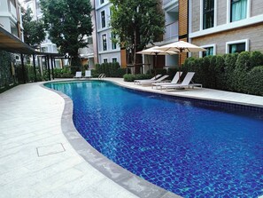 Una piscina interior moderna con agua azul cristalina, rodeada de sillones y sombrillas, ubicada en un patio con edificios de varios pisos.