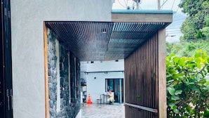 A modern building with a stone wall, a covered walkway, and a view of a residential area. - The Title V by The Esquire (Rawai)
