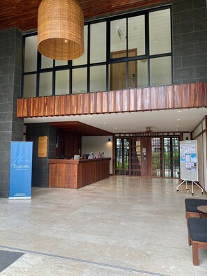 Un área de recepción con un mostrador de madera, una lámpara colgante grande y un cartel azul.