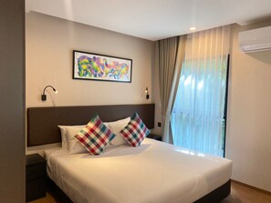 Habitación de hotel con una cama grande, dos almohadas, una obra de arte enmarcada, una ventana con cortinas y un equipo de aire acondicionado.