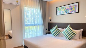 A hotel room with a large bed, a window with sheer curtains, a wall-mounted air conditioner, and a colorful abstract painting. - The Title V by The Esquire (Rawai)