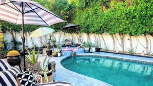 Un área junto a la piscina con sillones de descanso, sombrillas y plantas en macetas.