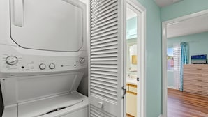 Een wasserette met een voorlader wasmachine en droger, een deur naar een badkamer, en een houten vloer.