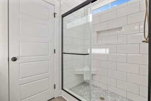 Ein Badezimmer mit weiß gefliesten Wänden, einer Duschkabine aus Glas und einer weißen Tür.