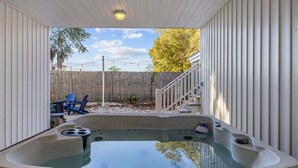 A hot tub in a covered outdoor area with a wooden fence and chairs in the background.