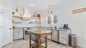 A kitchen with white walls, wooden flooring, a central island, and pendant lighting.