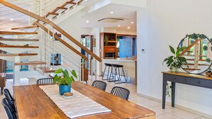 A modern interior with a wooden dining table, chairs, a staircase, and a kitchen area.