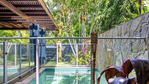 A glass-enclosed pool with a stone wall and tropical plants.