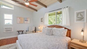Ein Schlafzimmer mit einem großen Bett, einem Sessel, einem Schreibtisch und einem Fenster mit Vorhängen.