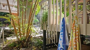 Ein tropischer Garten mit Bambuspflanzen und einem Duschbereich, an dem Handtücher auf einem Gestell hängen.