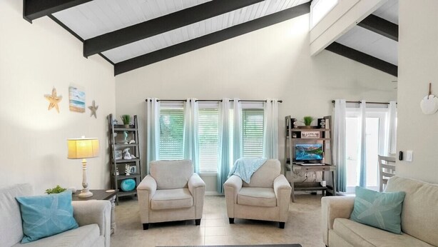 A living room with two beige armchairs, a coffee table with decorative items, a TV stand with a flat-screen TV, and a bookshelf. - Sarasota Coastal Style - Minutes To Siesta Beaches - Casa de Suenos (Sarasota)