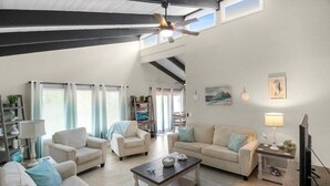 A spacious living room with a high ceiling, a ceiling fan, and a large window. There are two sofas, a coffee table, and a TV. - Sarasota Coastal Style - Minutes To Siesta Beaches - Casa de Suenos (Sarasota)