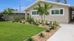 A residential house with a well-maintained lawn, a small garden with various plants, and a clear blue sky. - Sarasota Coastal Style - Minutes To Siesta Beaches - Casa de Suenos (Sarasota)