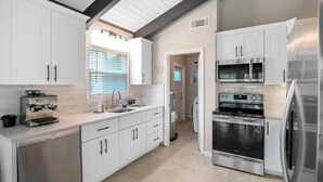 A modern kitchen with white cabinets, stainless steel appliances, and a window with blinds. - Sarasota Coastal Style - Minutes To Siesta Beaches - Casa de Suenos (Sarasota)