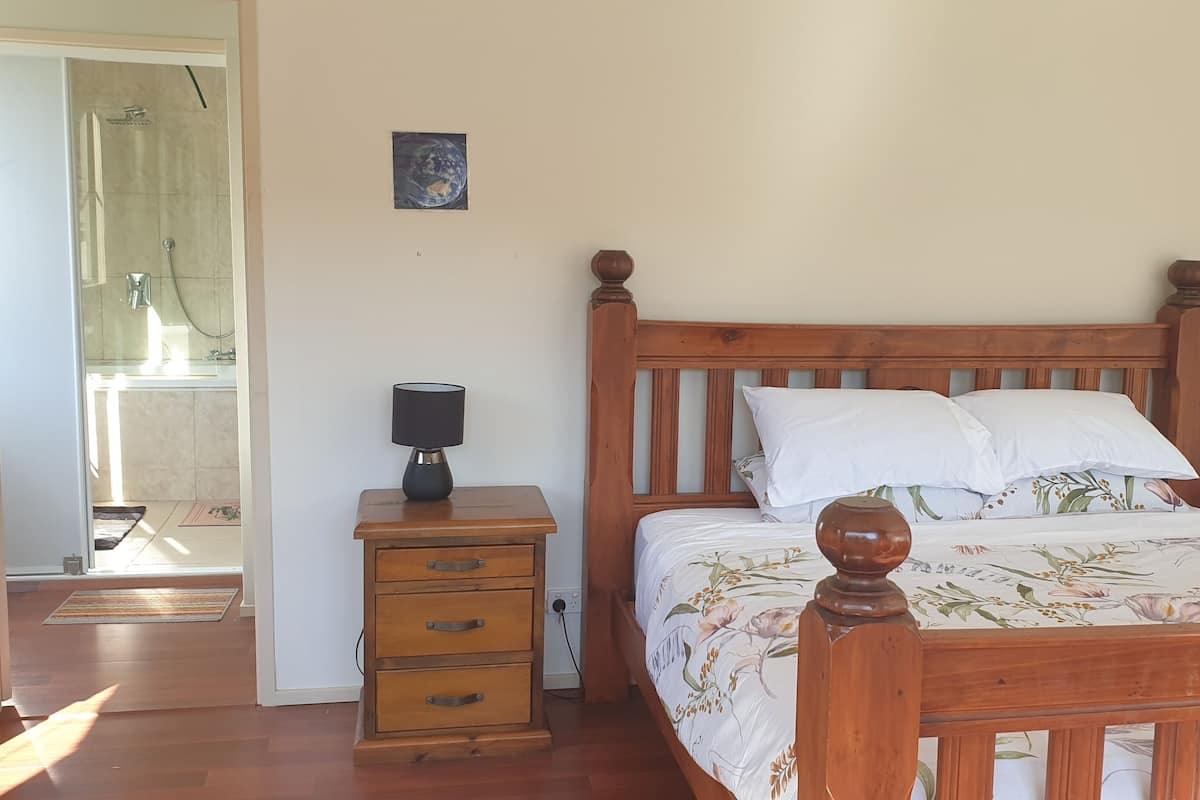 Una camera da letto con un letto in legno, due comodini con lampade, un mobiletto con cassetti, un mappamondo appeso al muro e vista sul bagno.