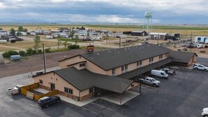 Un edificio grande con techo plano, varios espacios de estacionamiento y un tanque de agua al fondo.