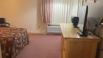 A bedroom with a bed, a desk, a computer, and a window with curtains.
