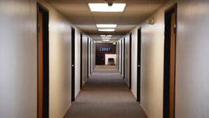 Un largo y estrecho pasillo de hotel con puertas a ambos lados y suelo alfombrado.