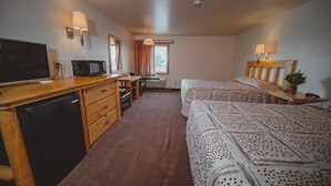 Habitación de hotel con escritorio de madera, televisión, microondas, dos camas con ropa de cama estampada y ventana con cortinas.