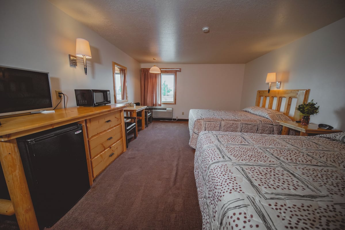 Habitación de hotel con escritorio de madera, televisión, microondas, dos camas con ropa de cama estampada y ventana con cortinas.
