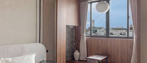 A modern hotel room with a large window, a bed, a small table, and a vase.