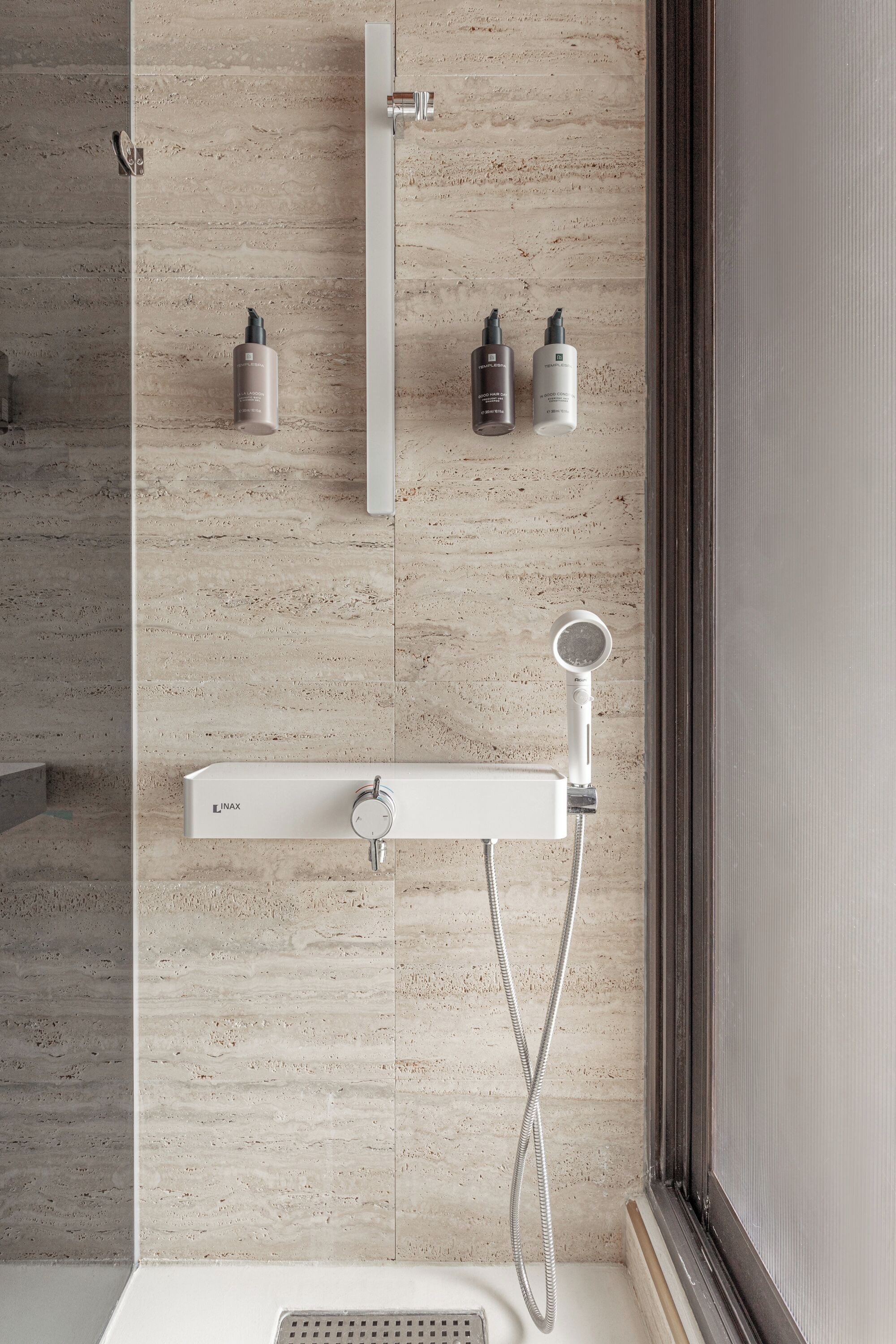 A modern bathroom with a built-in shower, a wall-mounted soap dispenser, and a handheld showerhead.