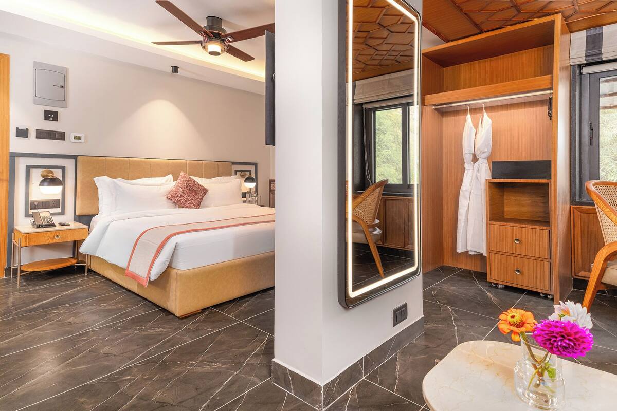 A modern hotel room with a large bed, a ceiling fan, a bathroom with wooden cabinets, and a large mirror.