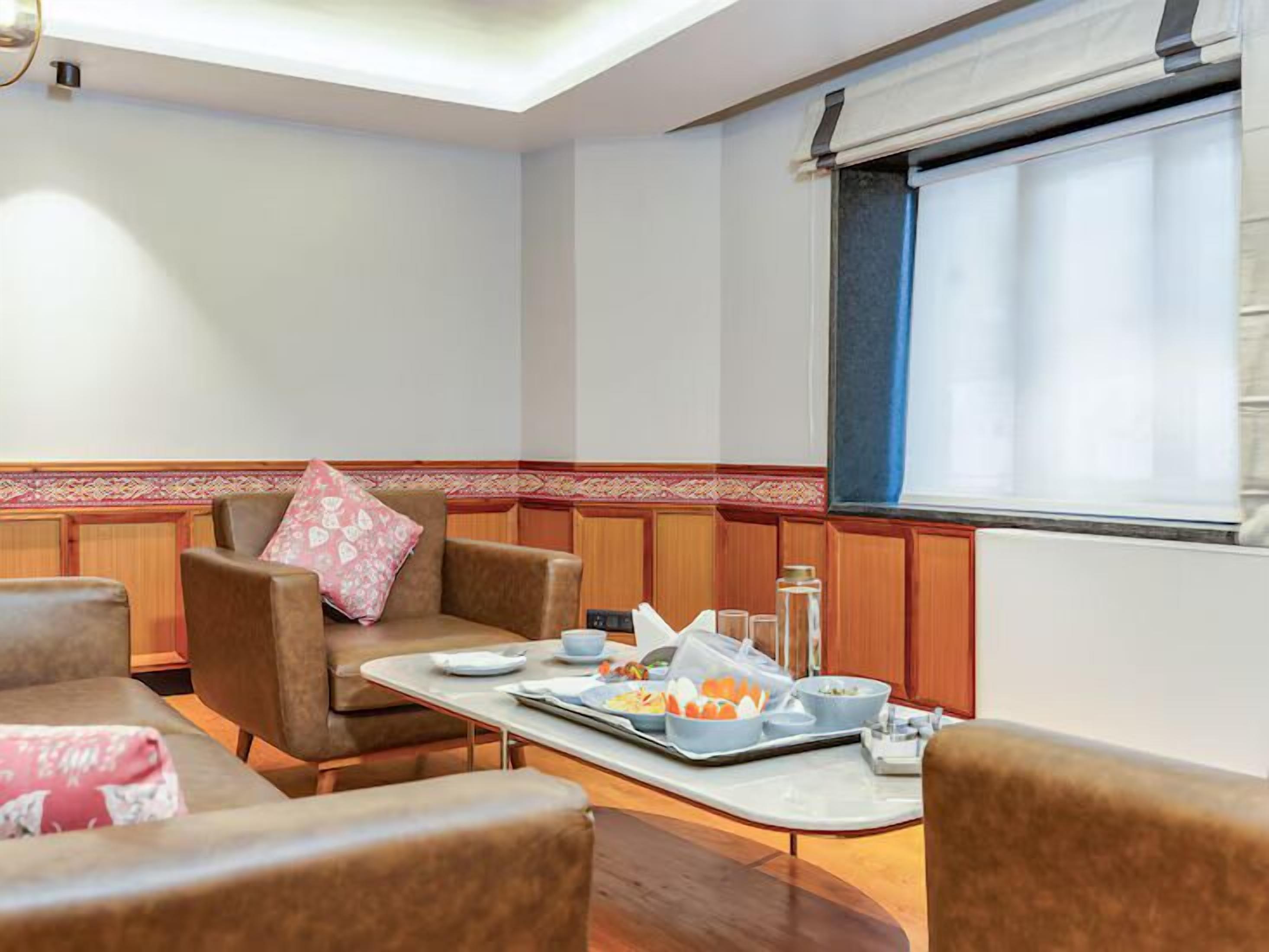 A dining area with a table set for two, two cushioned chairs, a decorative border, and a window with blinds.
