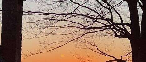 Zonsondergang boven een bergachtig landschap, te zien vanaf een balkon van een gebouw.