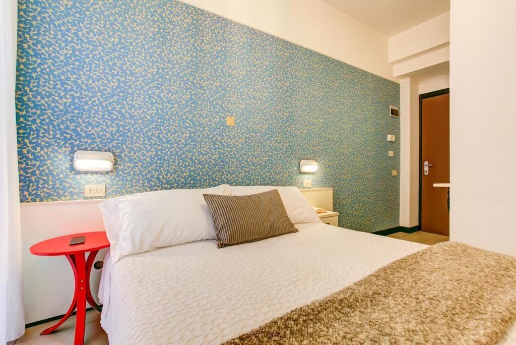 A hotel room with a bed, a red side table, and a patterned wall.
