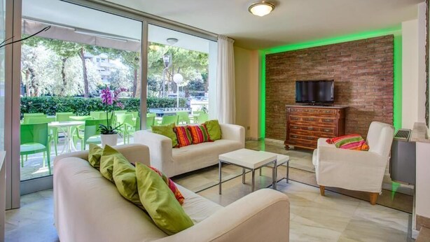 A modern living room with a sofa, armchair, and a TV on a brick wall. - HOTEL KONRAD (Rimini)
