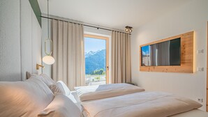 Une chambre d’hôtel avec deux lits, une grande fenêtre donnant sur les montagnes, un téléviseur fixé au mur et un luminaire au plafond.
