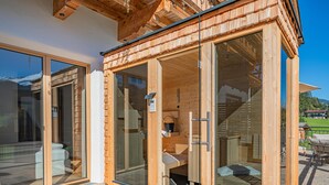 A wooden cabin with large sliding glass doors, a covered outdoor seating area, and a view of the surrounding landscape. - Exclusive apartments with garden and sauna (Hollersbach im Pinzgau)