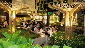 An outdoor dining area with people seated at tables, surrounded by greenery and under a canopy structure. - The Wellington-Republic Plaza Airport (Ho Chi Minh City)