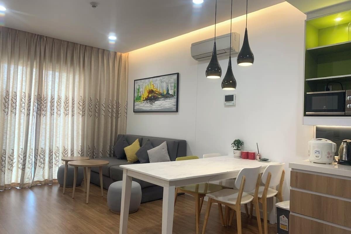 A modern living room with a sofa, dining table, and chairs. There is a kitchen area with a microwave and a green shelf.