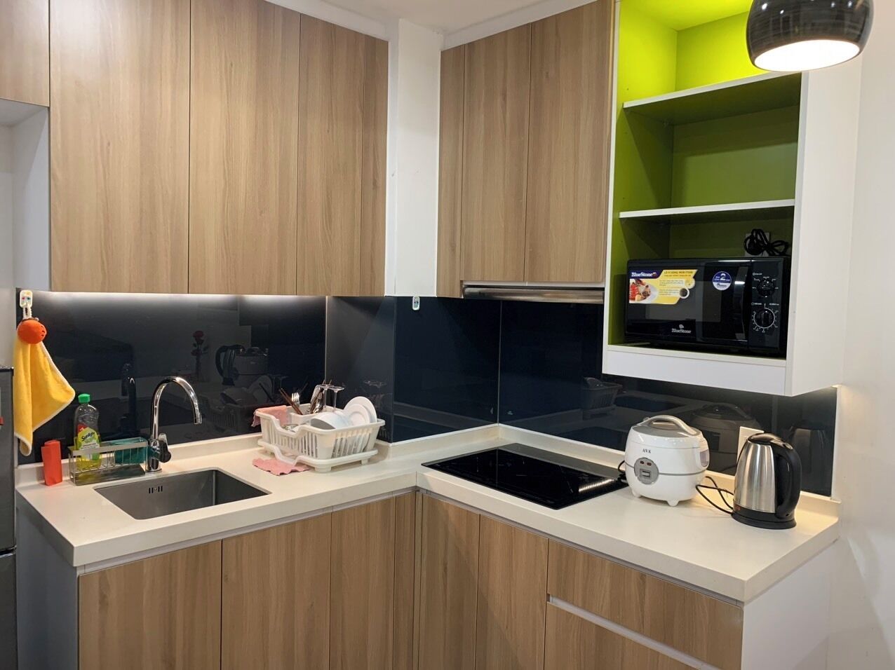 A modern kitchen with wooden cabinets, a black backsplash, a sink, a stove, and a kettle.