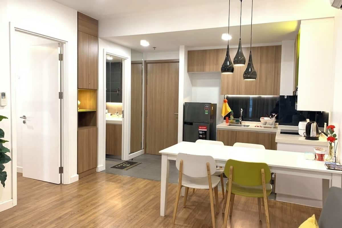 A modern kitchen with wooden cabinets, a white countertop, and a built-in oven. There is a dining area with a white table and chairs, and a kitchen island with a sink and a refrigerator.