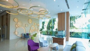 A modern lobby with circular wall decor, a seating area with colorful chairs, and a large window offering a view of greenery. - The Wellington-Republic Plaza Airport (Ho Chi Minh City)
