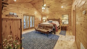 A wooden cabin bedroom with a bed, a sofa, a ceiling fan, and a window with blinds. - Private Cozy Cabin w/ Hot Tub in Blue Ridge! (Blue Ridge)