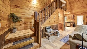 A wooden cabin interior with a staircase, a sofa, a lamp, and a kitchen area. - Private Cozy Cabin w/ Hot Tub in Blue Ridge! (Blue Ridge)